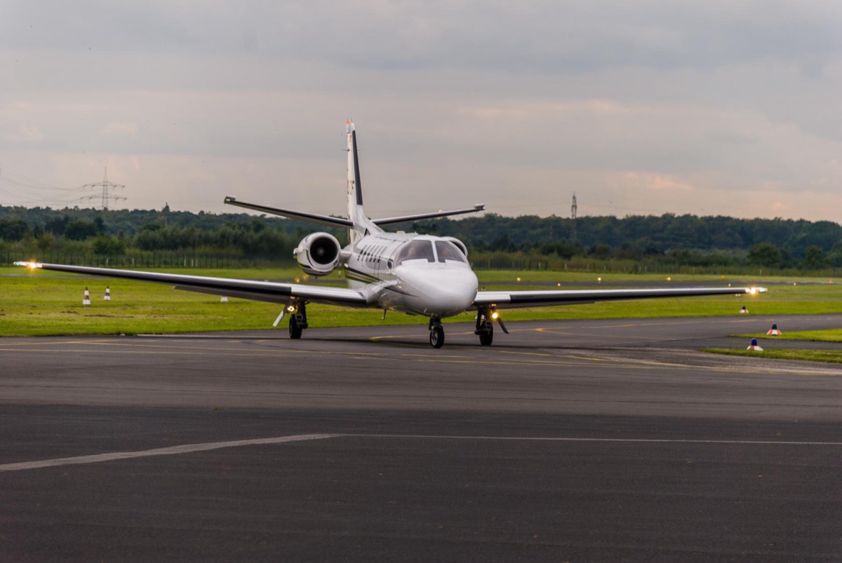 A light business jet taxiing toward the camera on a grass lined airfield under an overcast sky