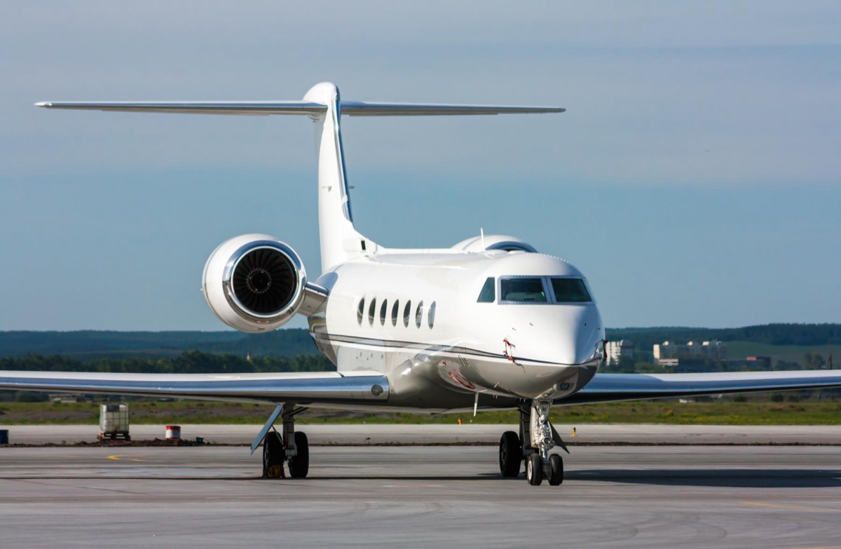 A large cabin business jet with oval windows parked on the ramp in clear weather, photographed from ahead of the wing