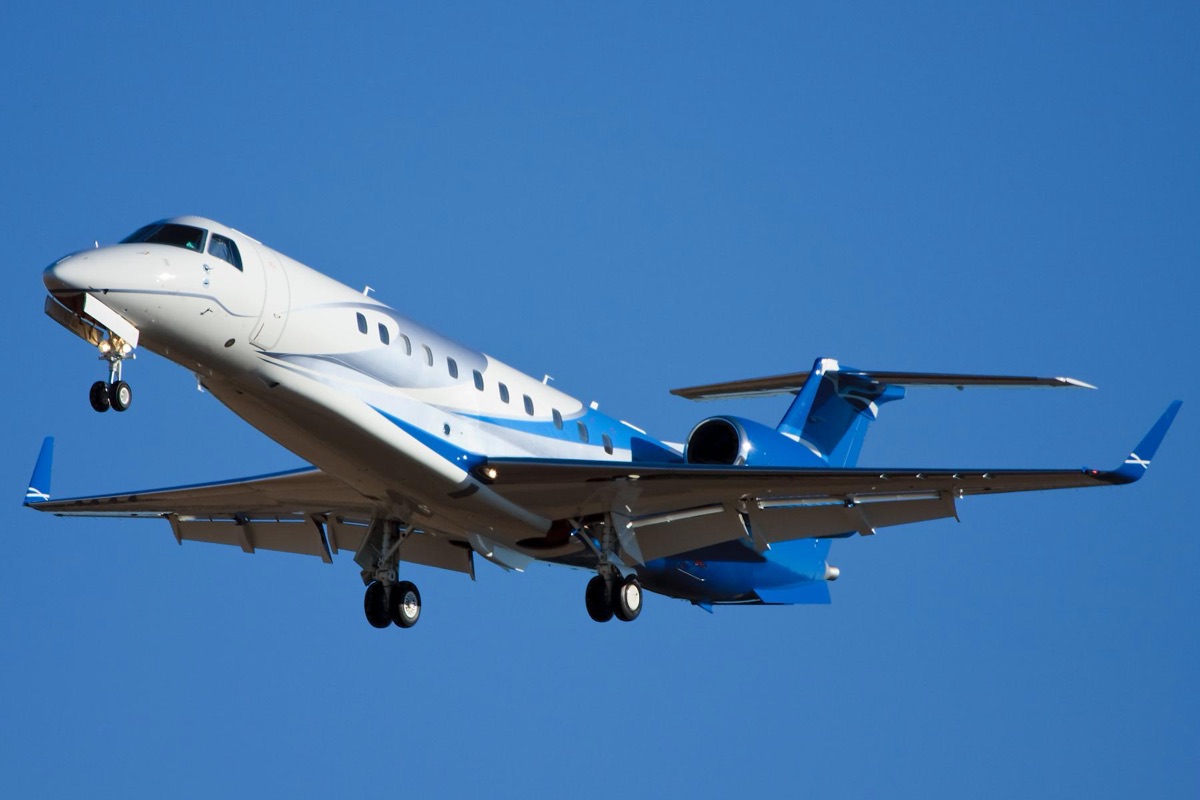 A white and blue business jet climbing away with the landing gear still extended against a clear blue sky