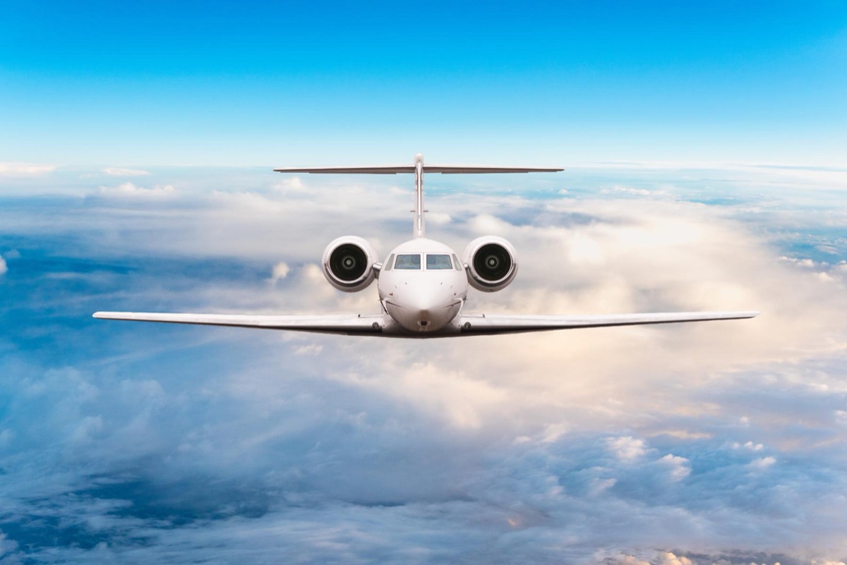 A business jet photographed head on in level flight above a layer of cumulus cloud