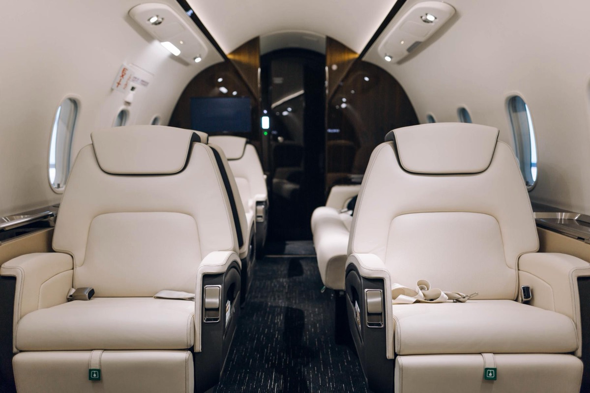 The interior of a private jet cabin looking aft along the aisle between four cream leather club seats