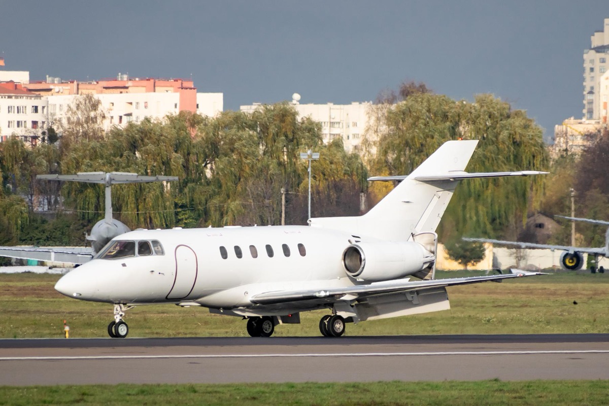 A midsize business jet on the landing roll with speed brakes deployed and a city skyline behind the airfield