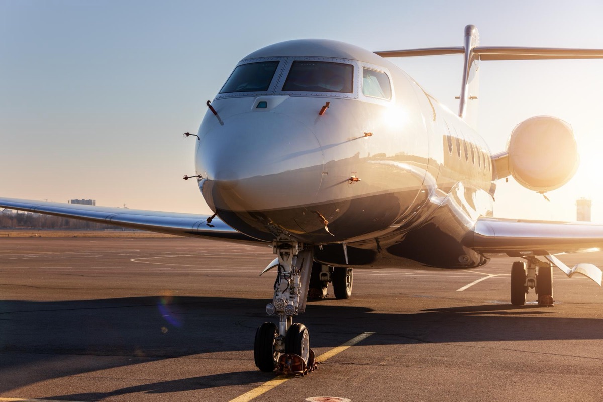 A business jet parked on an airport ramp at sunrise, backlit, with the nose gear and forward fuselage in the foreground
