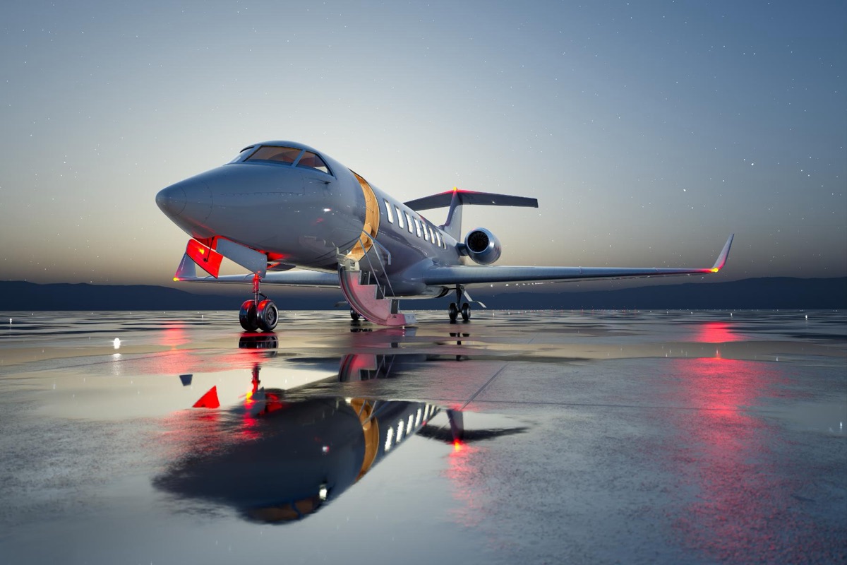 A business jet on a wet ramp at twilight with its navigation lights reflected in standing water and stars overhead