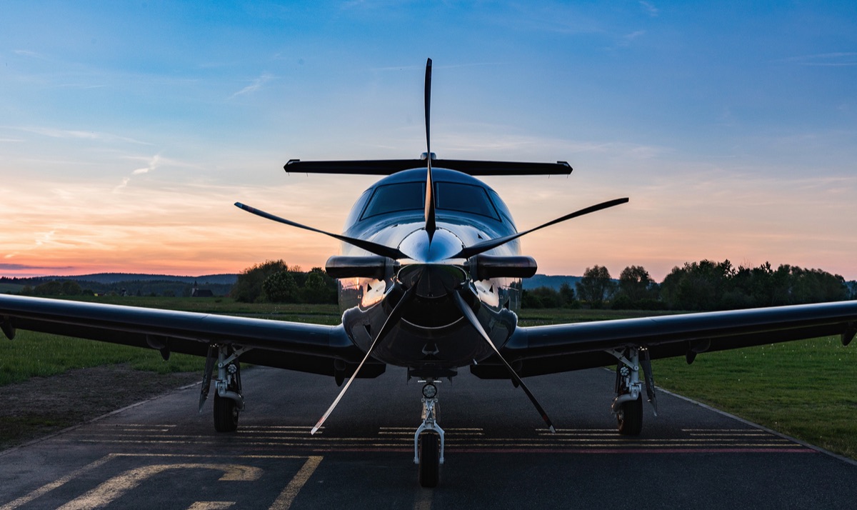 A Pilatus PC-12 single engine turboprop photographed head on at dusk on a rural airfield apron, five blade propeller stationary